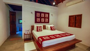 A bedroom with a large bed, white brick walls, wooden beams, and a red and white patterned bedspread. - Eliyanth Udawalawe (Udawalawa)