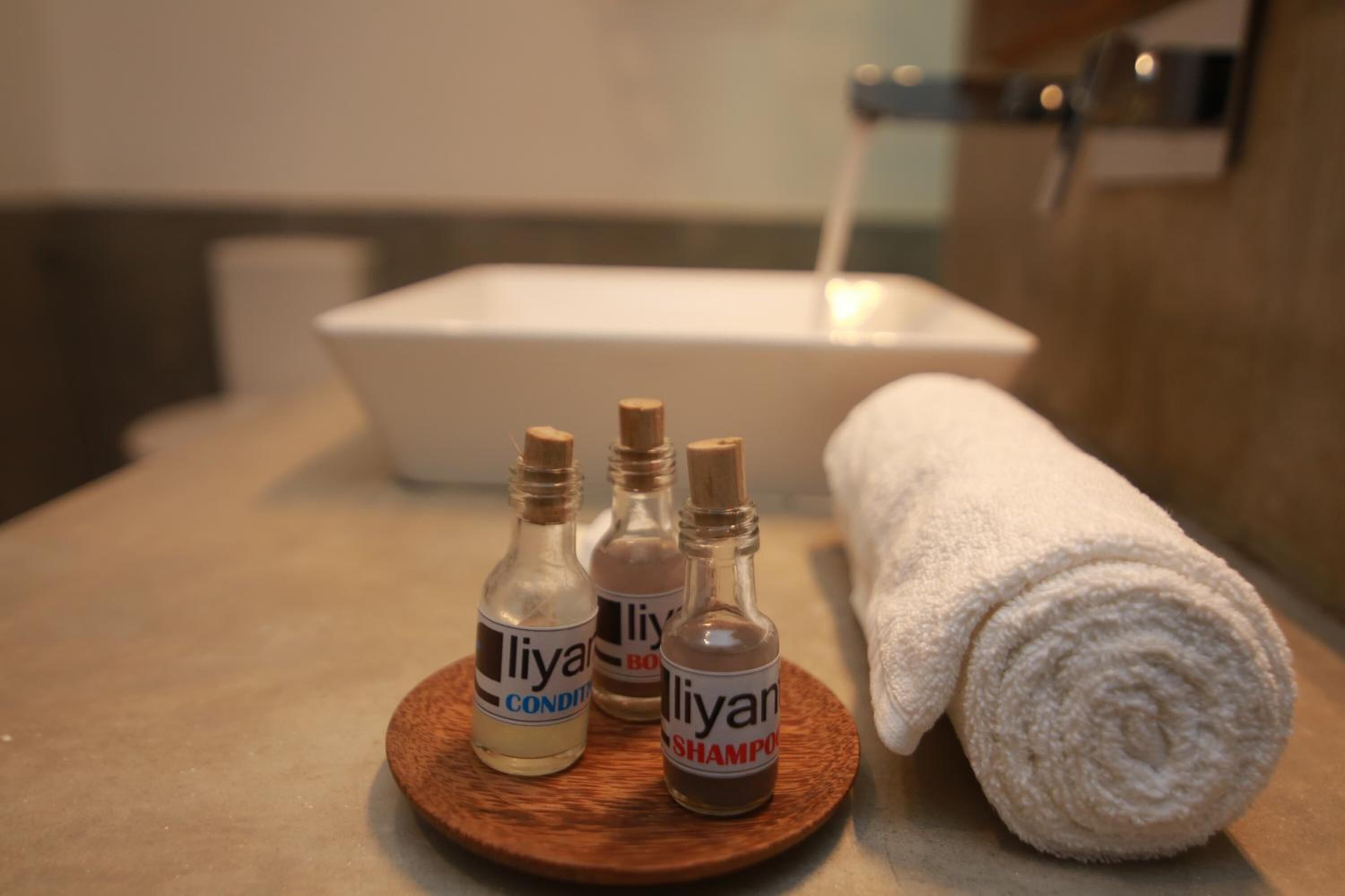 Un baño con un lavabo blanco, una toalla y tres productos 'Liyan' sobre una bandeja de madera.