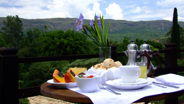 A table set with food and a teapot, overlooking a scenic landscape. - Lis Bleu Pousada (Tiradentes)
