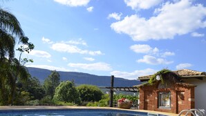A swimming pool with a clear view of mountains in the background, surrounded by lush greenery and a pergola with plants. - Lis Bleu Pousada (Tiradentes)