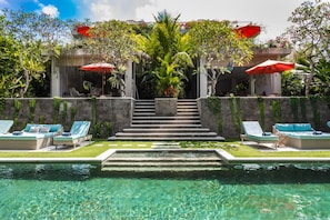 A poolside area with lounge chairs, a staircase leading to a covered area, and a clear pool.