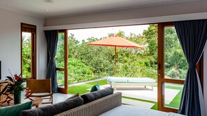 Ein Schlafzimmer mit einem großen Bett, einem Schlafsofa, einem Sessel und Blick auf einen Garten durch eine Glastür.