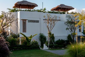 Un bâtiment moderne à l’extérieur blanc, doté d’une porte en bois et de deux parasols à toiture de chaume sur le toit.