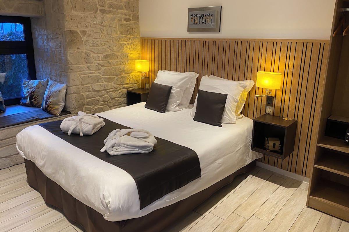 Een hotelkamer met een groot bed, twee bedlampen, een stenen muur, een houten hoofdeinde en een ingelijst schilderij aan de muur.