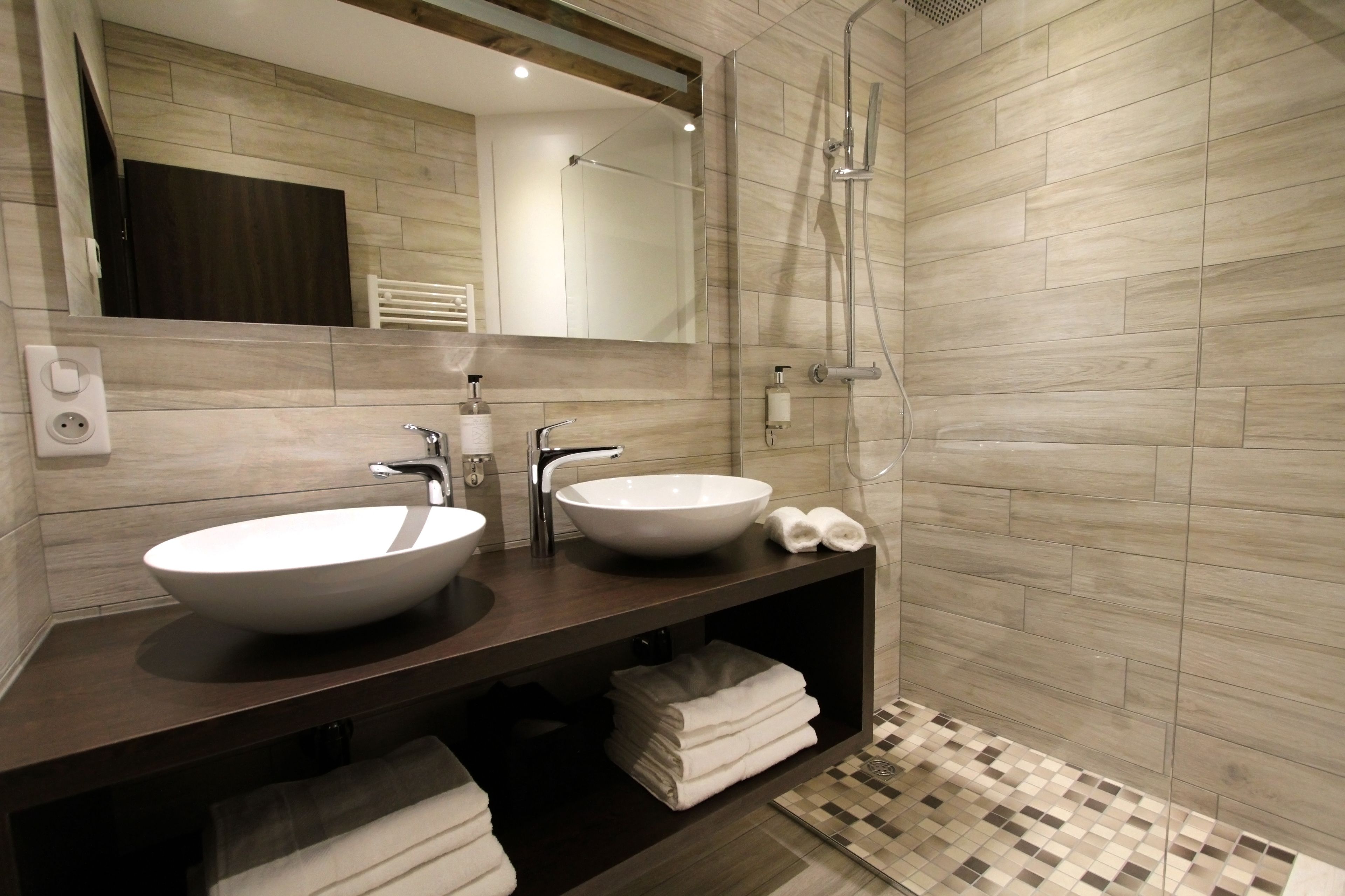A modern bathroom with two sinks, a shower, and a mirror.