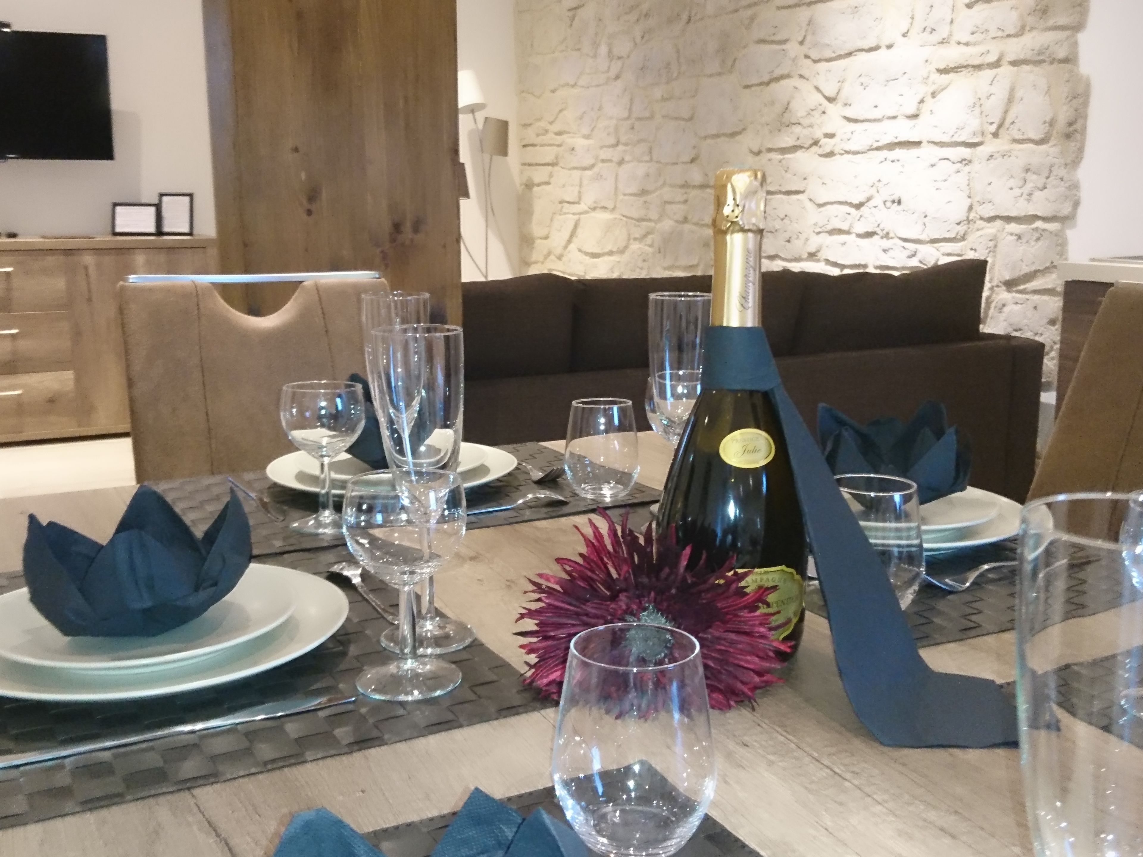 Een eettafel gedekt met wijnglazen, borden en een champagnefles.
