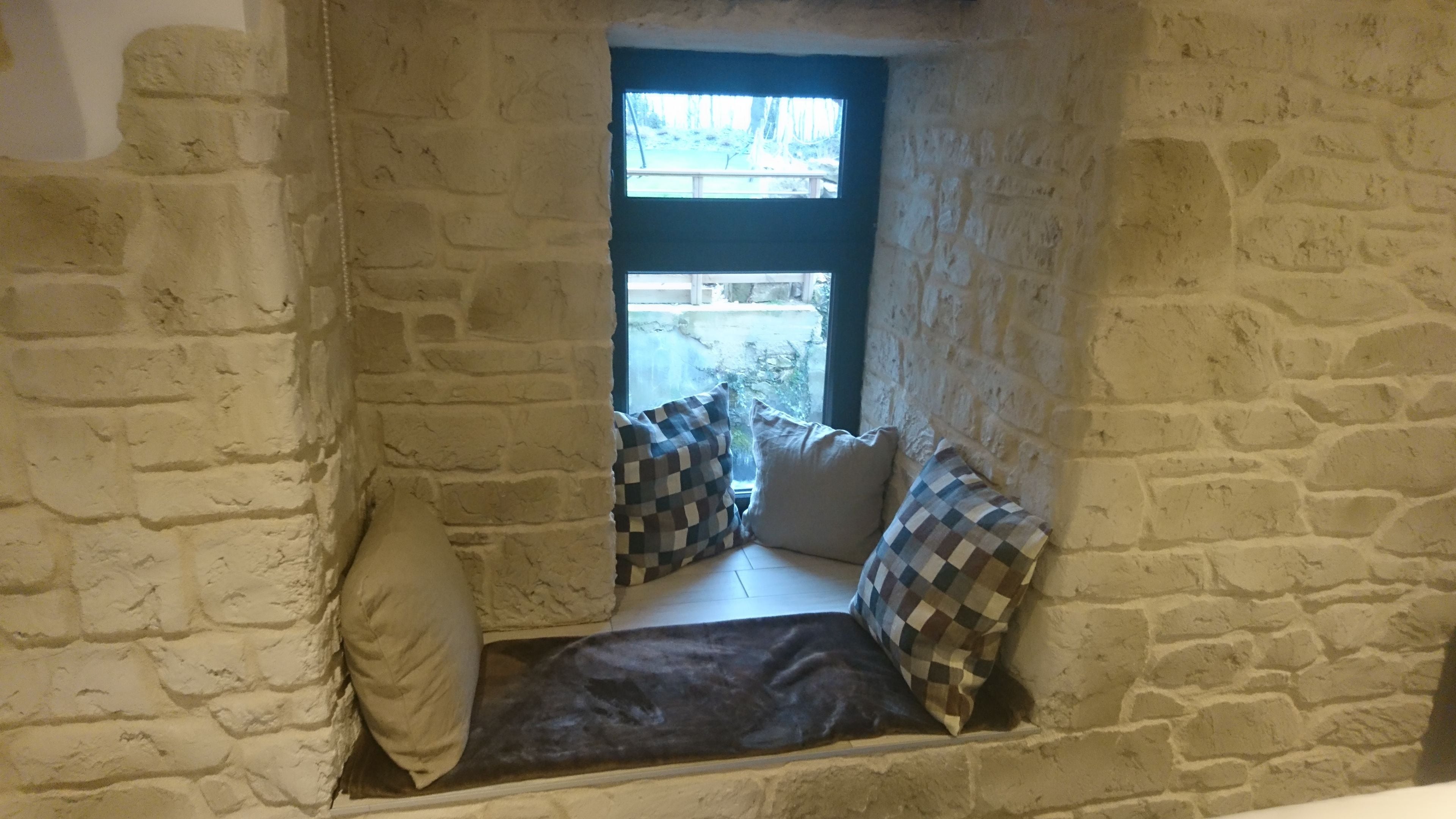 A small, stone-walled room with a window, a bench, and two checkered cushions.