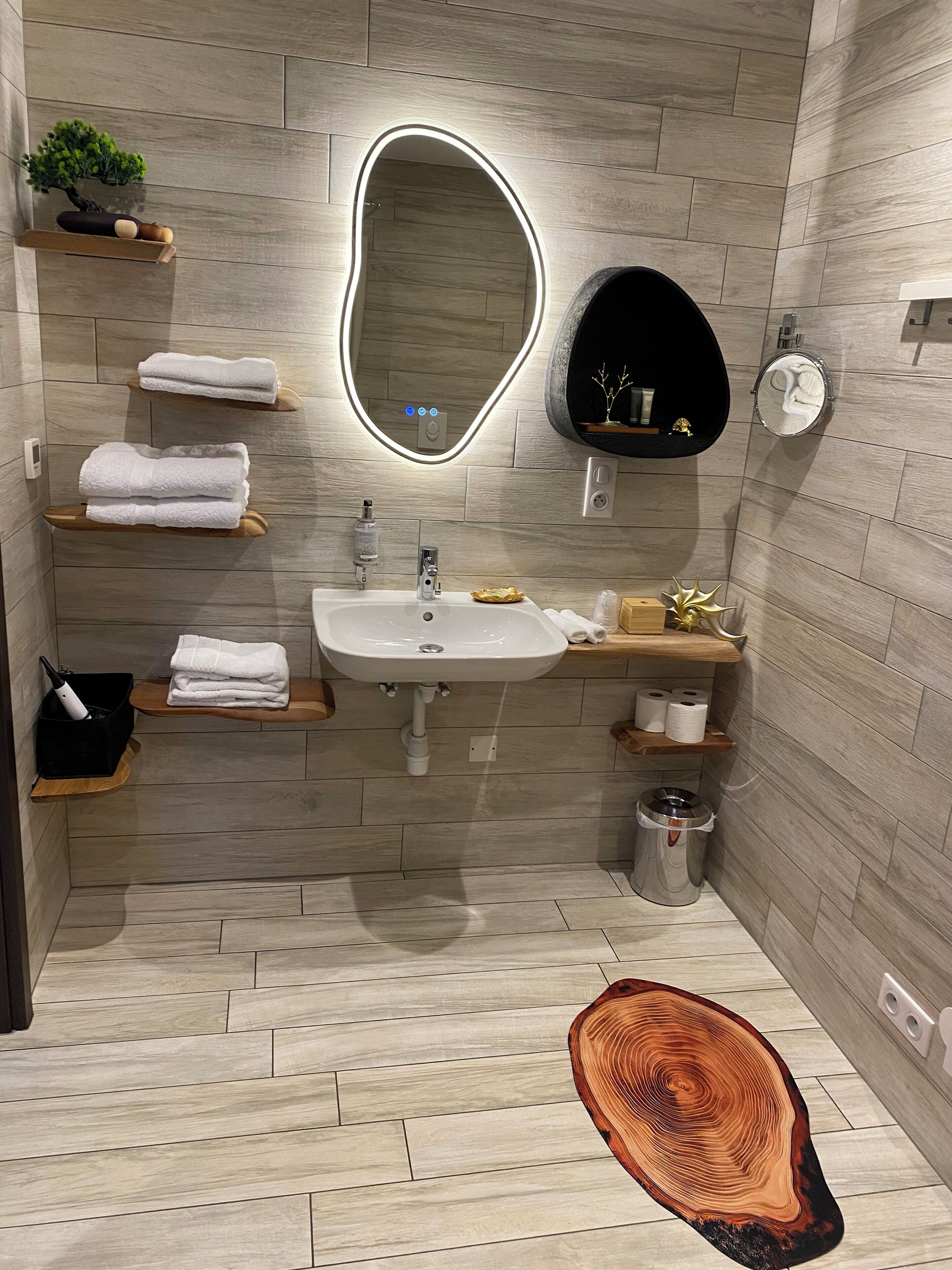 A modern bathroom with a sink, mirror, towel racks, and a trash can.