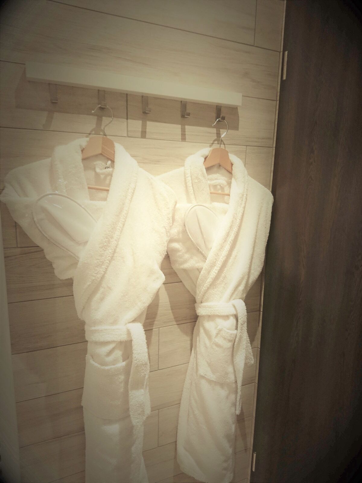 Two white bathrobes hanging on a wooden rack in a bathroom.