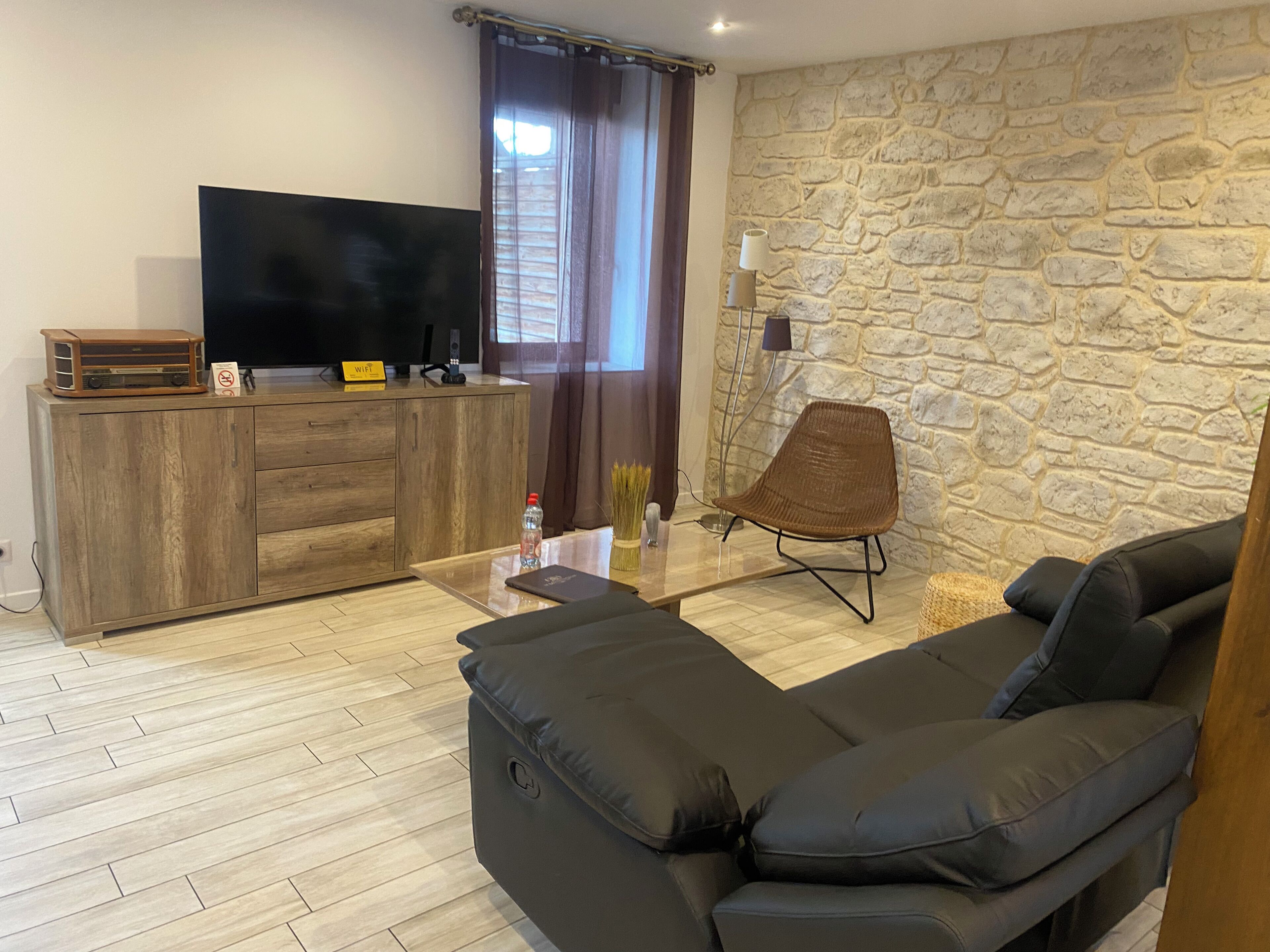 Ein modernes Wohnzimmer mit Steinwand, Flachbildfernseher, Holzschrank, schwarzem Sofa und Korbstuhl.
