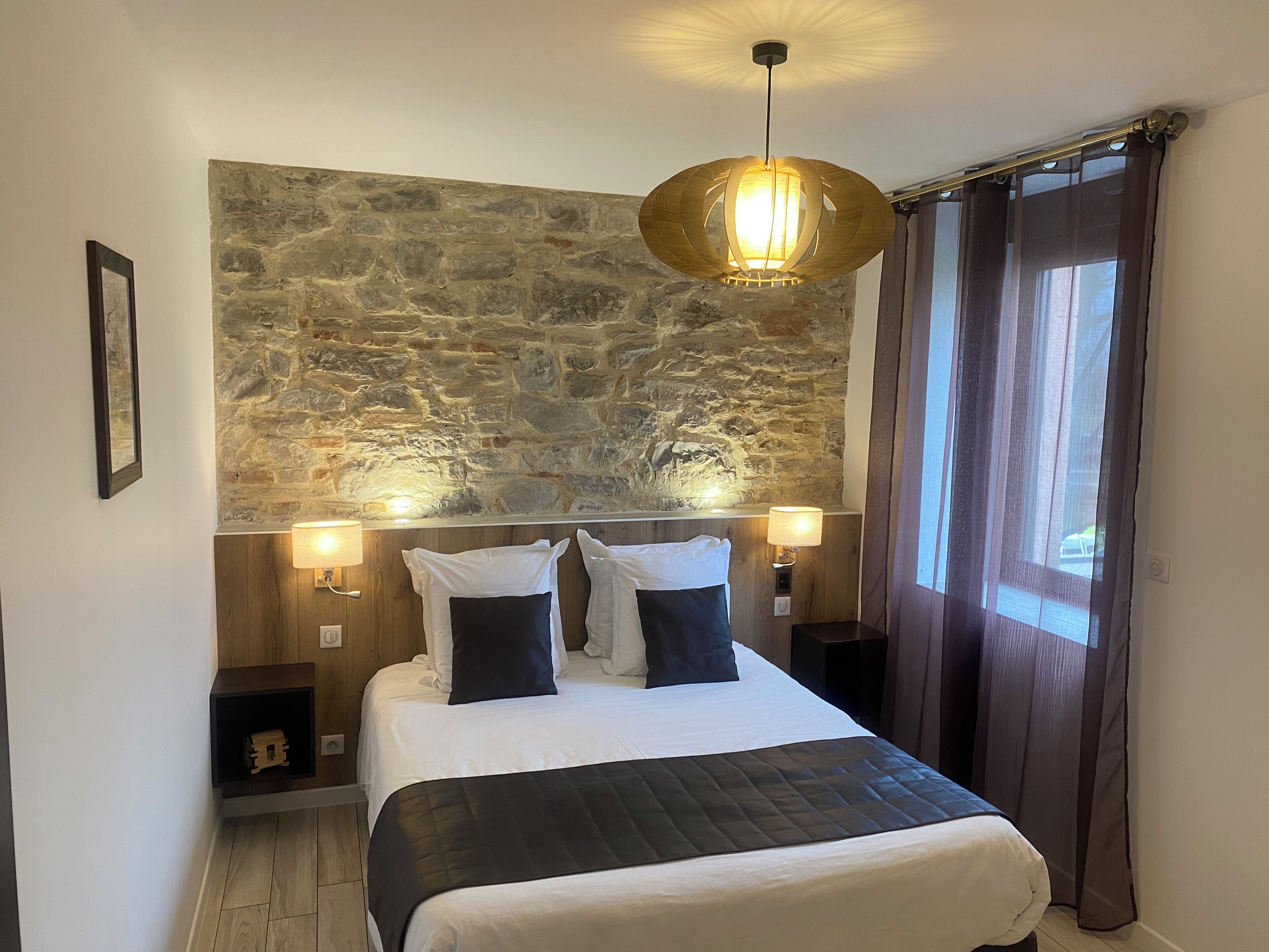 A bedroom with a stone wall, a bed with white bedding, two bedside lamps, and a hanging light fixture.