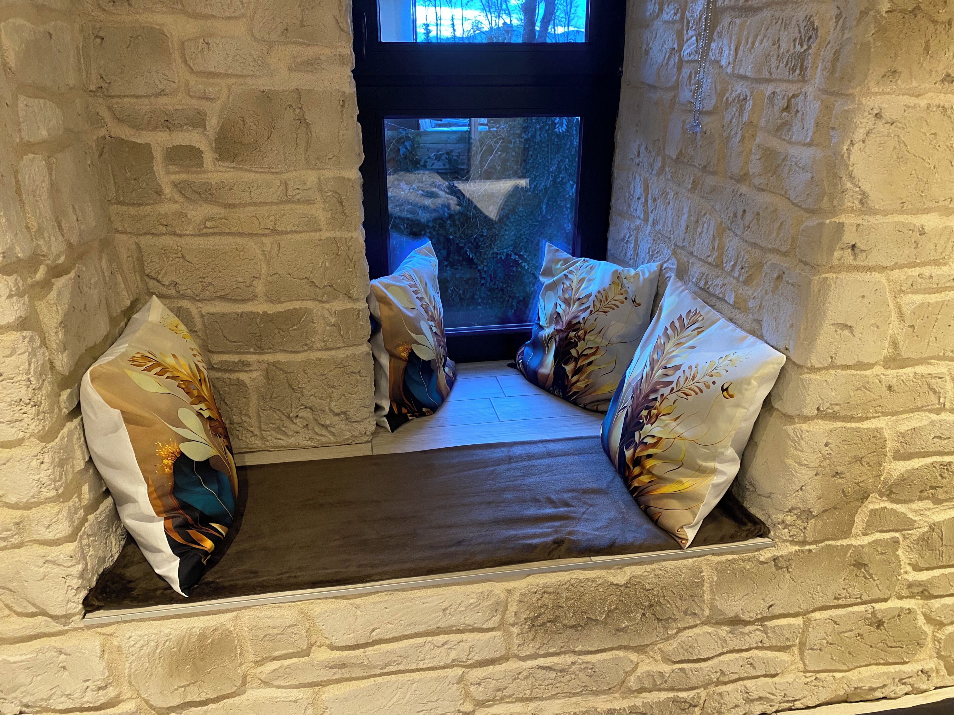 A stone-walled room with a bench and two pillows with leaf patterns.