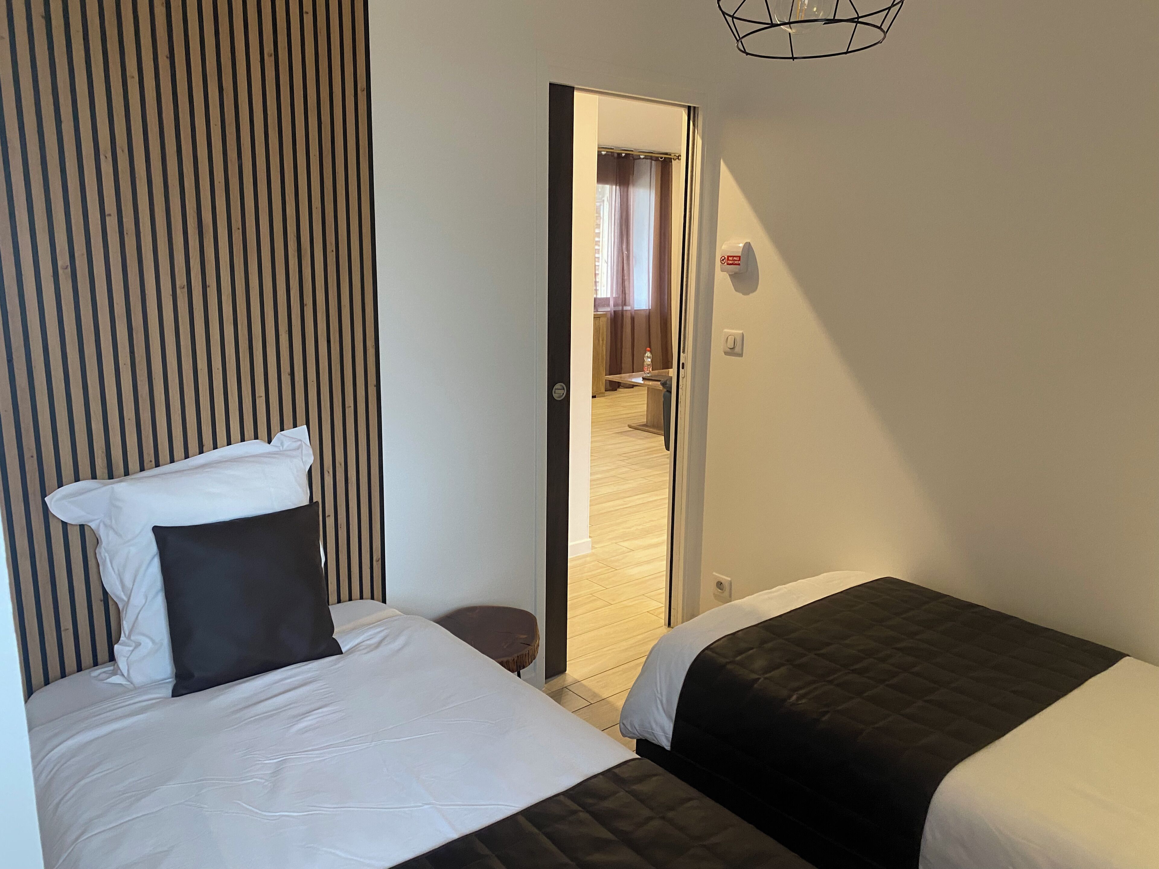 A hotel room with two beds, a wooden slat headboard, a small round table, and a door leading to a bathroom.