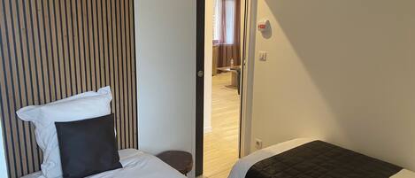 A hotel room with two beds, a wooden slat headboard, a small round table, and a door leading to a bathroom.