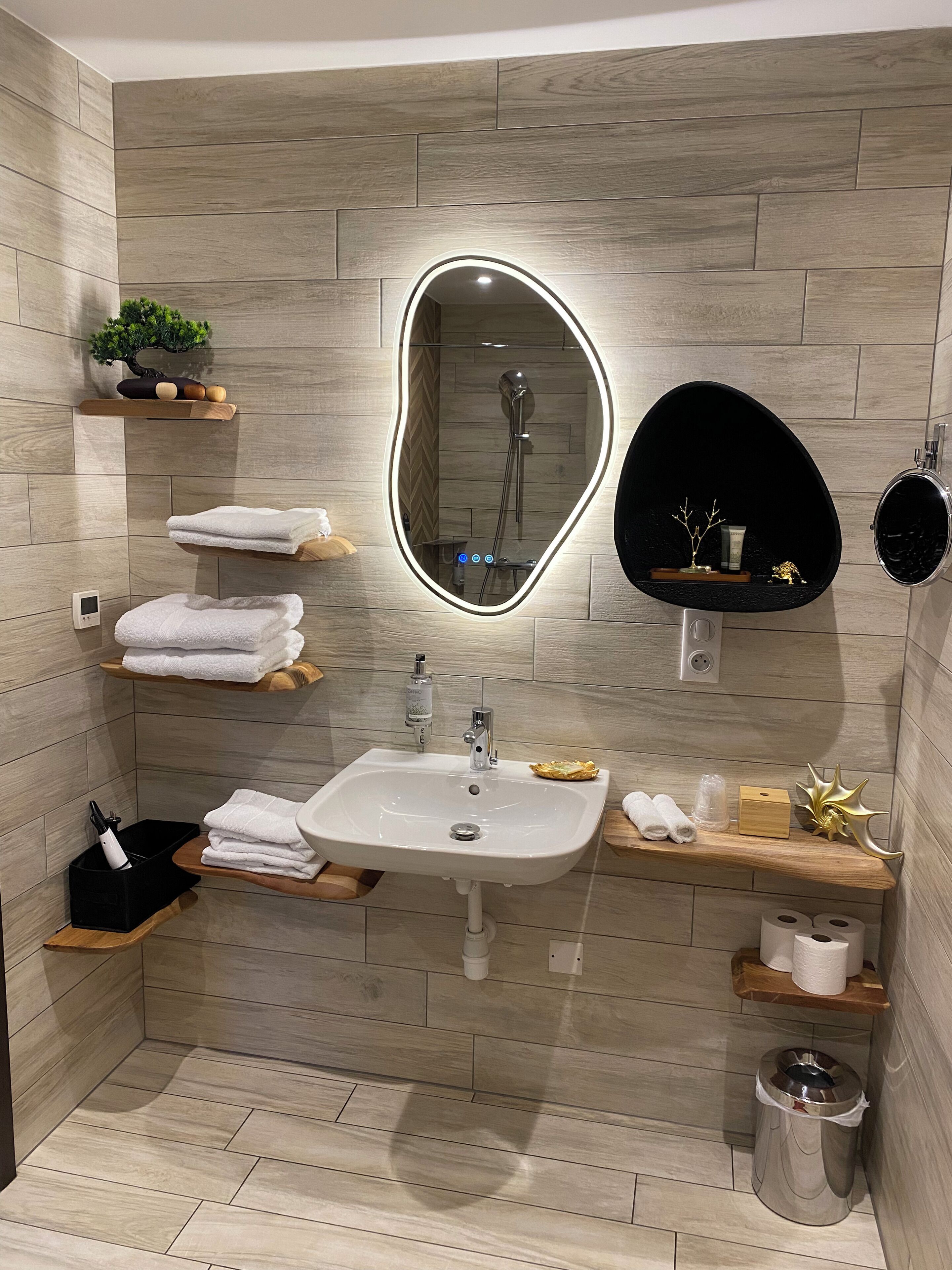 A modern bathroom with a sink, mirror, shower, and various toiletries.