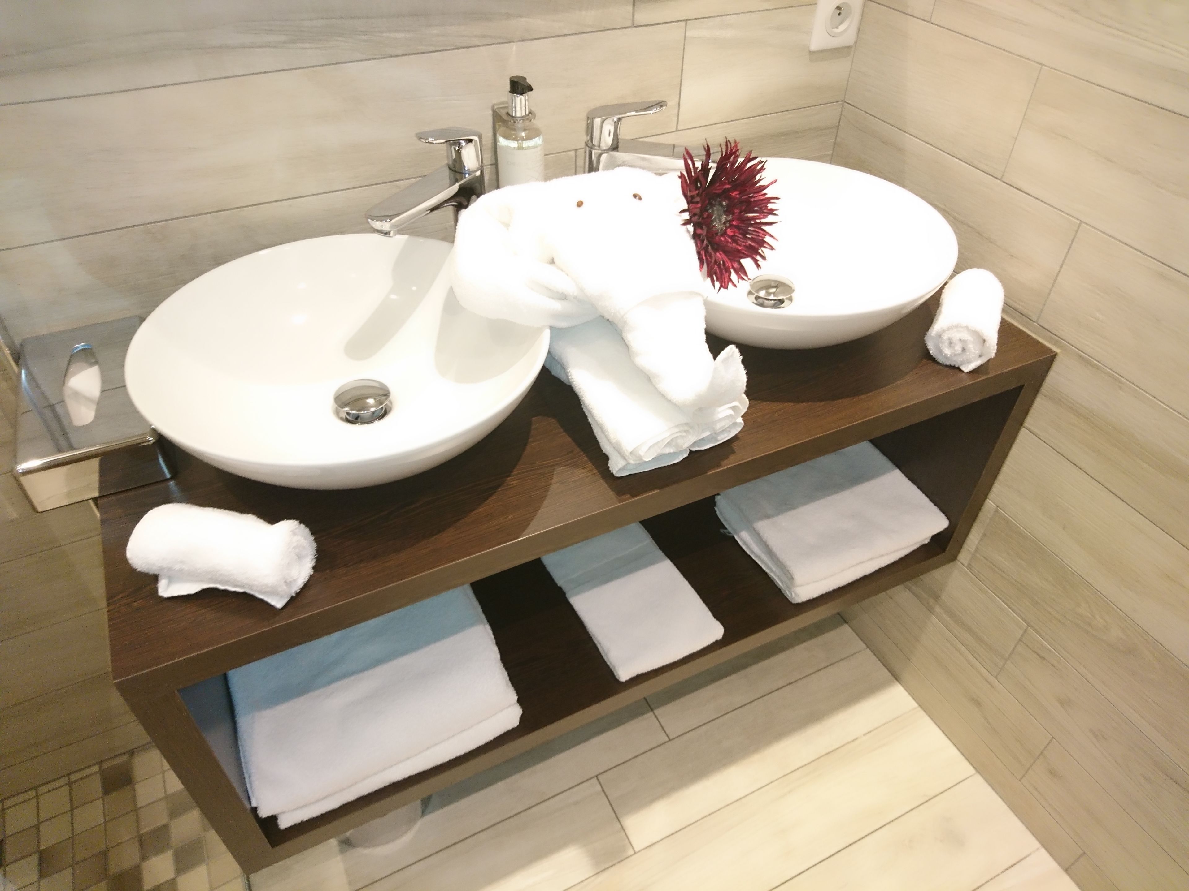 Une salle de bain avec deux lavabos, un miroir et un porte-serviettes où sont pliées des serviettes.