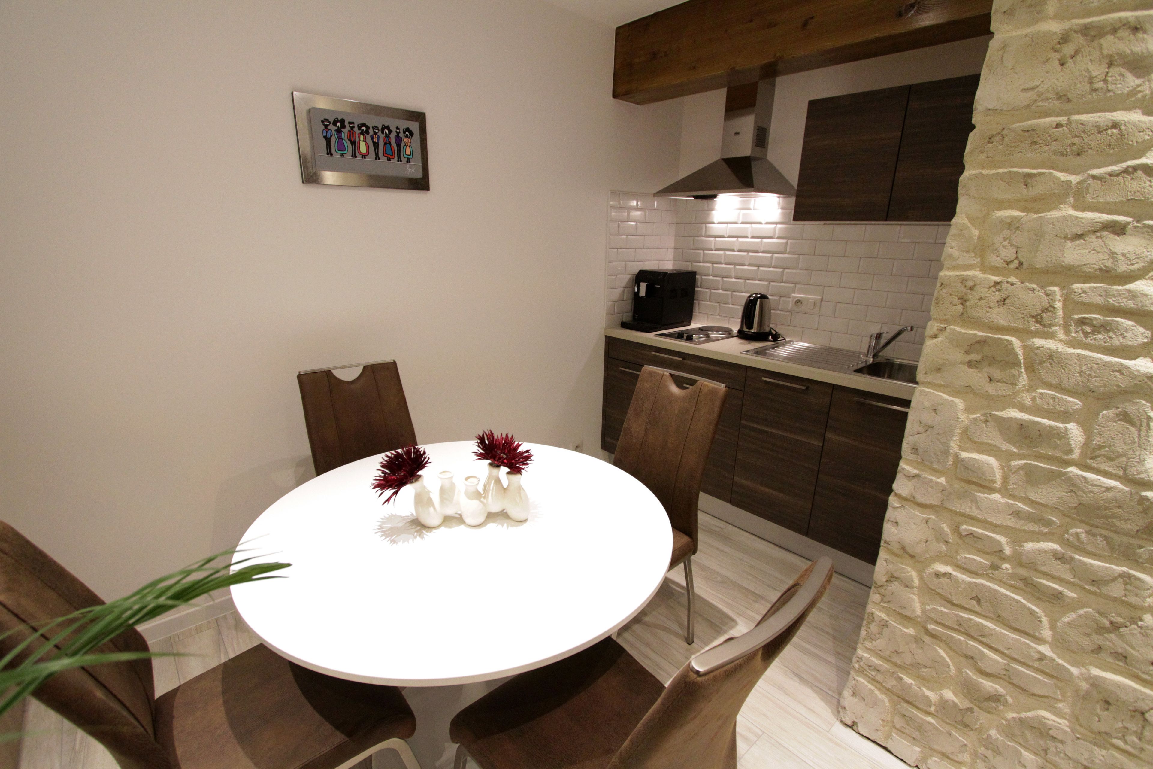 Zona pranzo con tavolo rotondo e sedie, cucina sullo sfondo e parete in pietra.