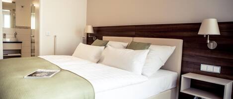 A neatly made bed with a green blanket, two bedside lamps, and a small bedside table.