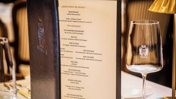 A menu in a restaurant setting with a wine glass and cutlery on the table.
