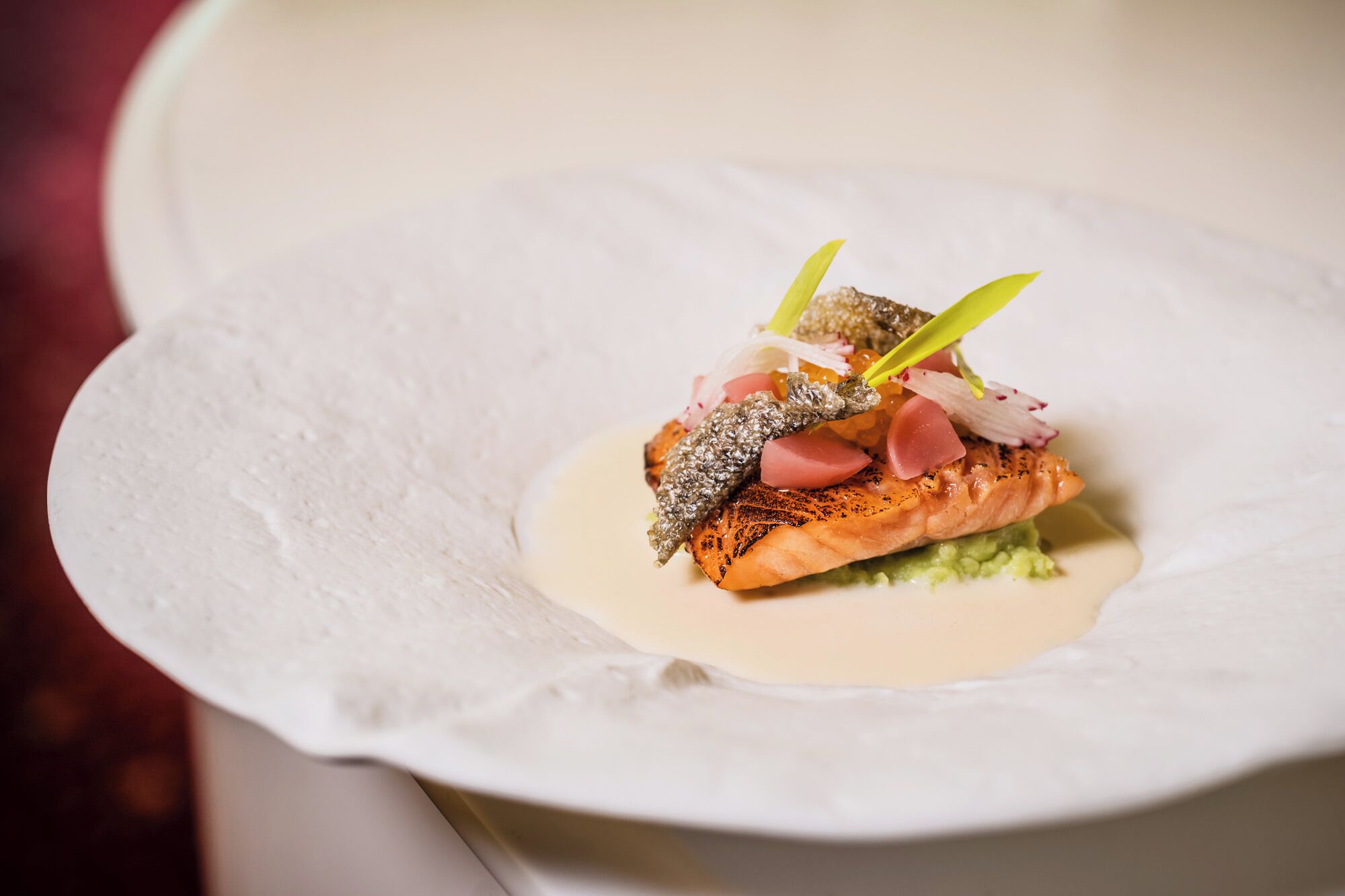 Un plato de salmón con guarniciones y salsa cremosa en un tazón blanco.