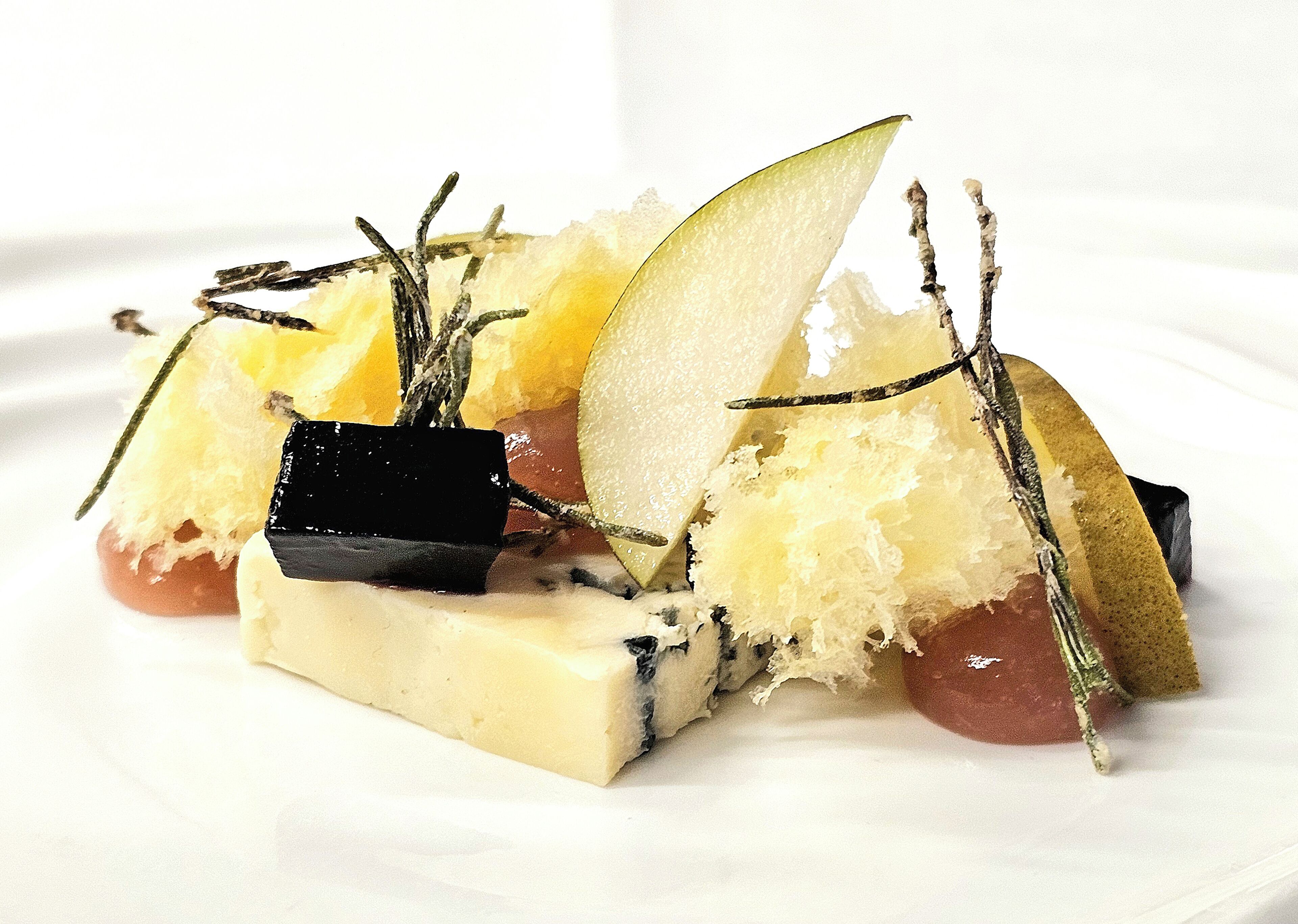 Un plato de postre con una porción de pastel, fruta y adornos decorativos.