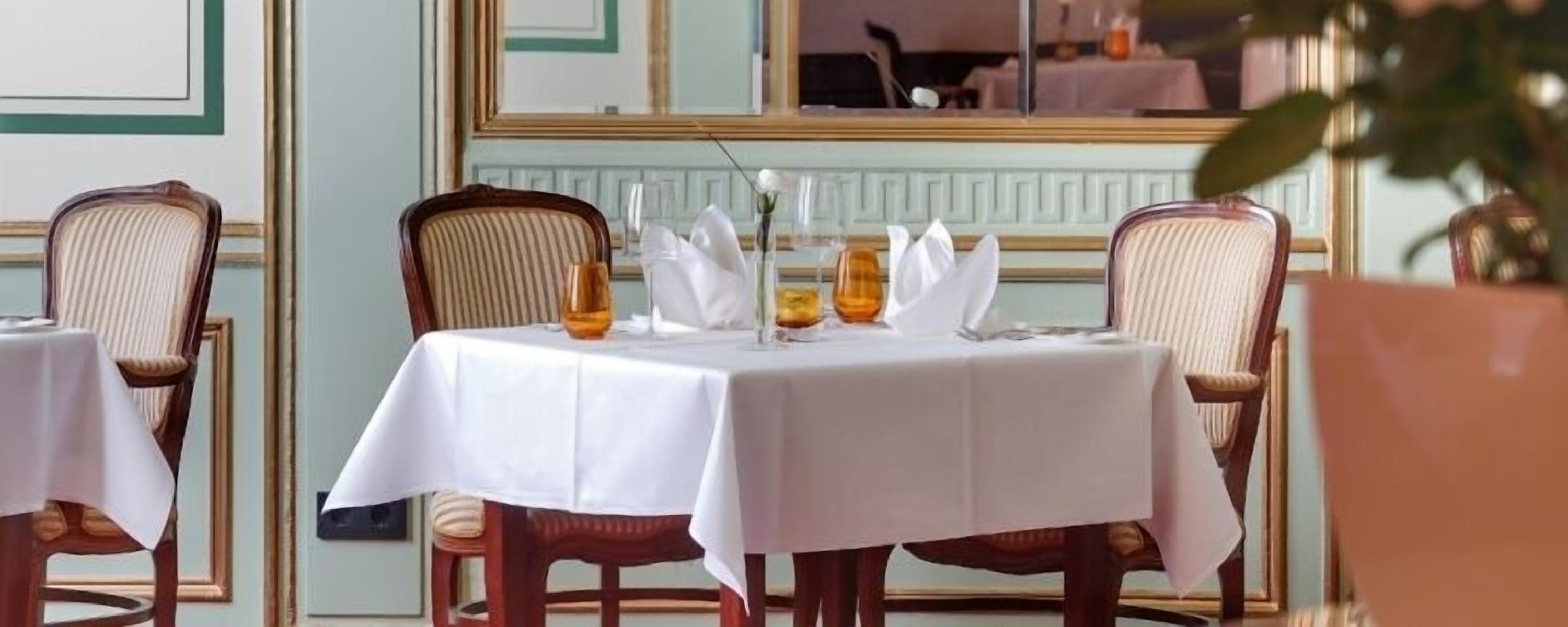 A dining table set with white tablecloths, chairs, and a vase with flowers.