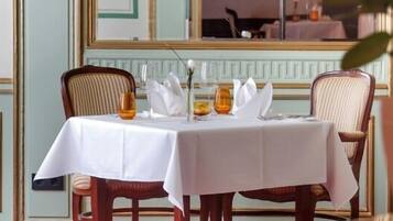 A dining table set with white tablecloths, chairs, and a vase with flowers.