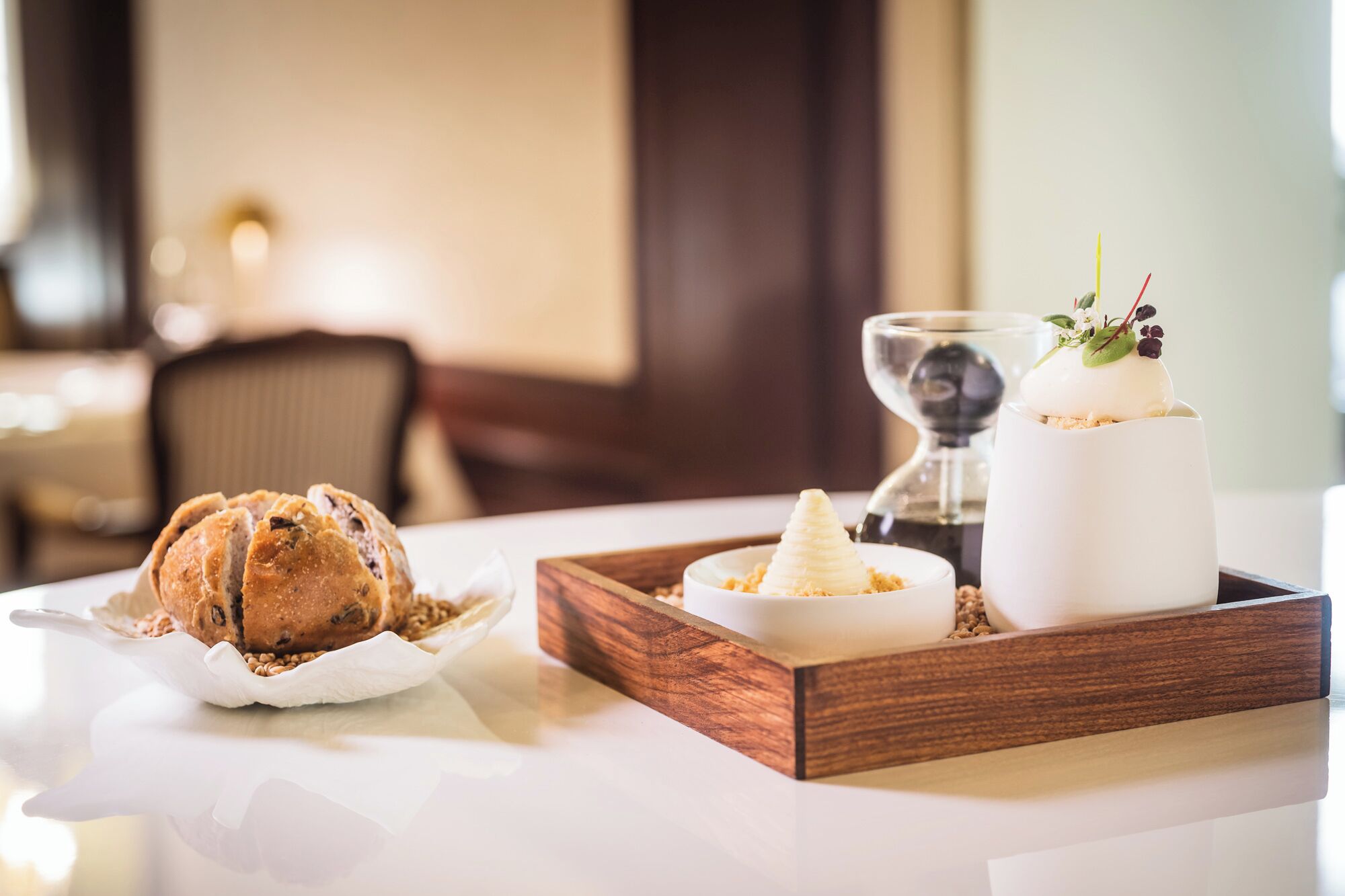 A dessert tray with a croissant, a scoop of ice cream, and a white dessert topped with a leaf and berry on a wooden tray.