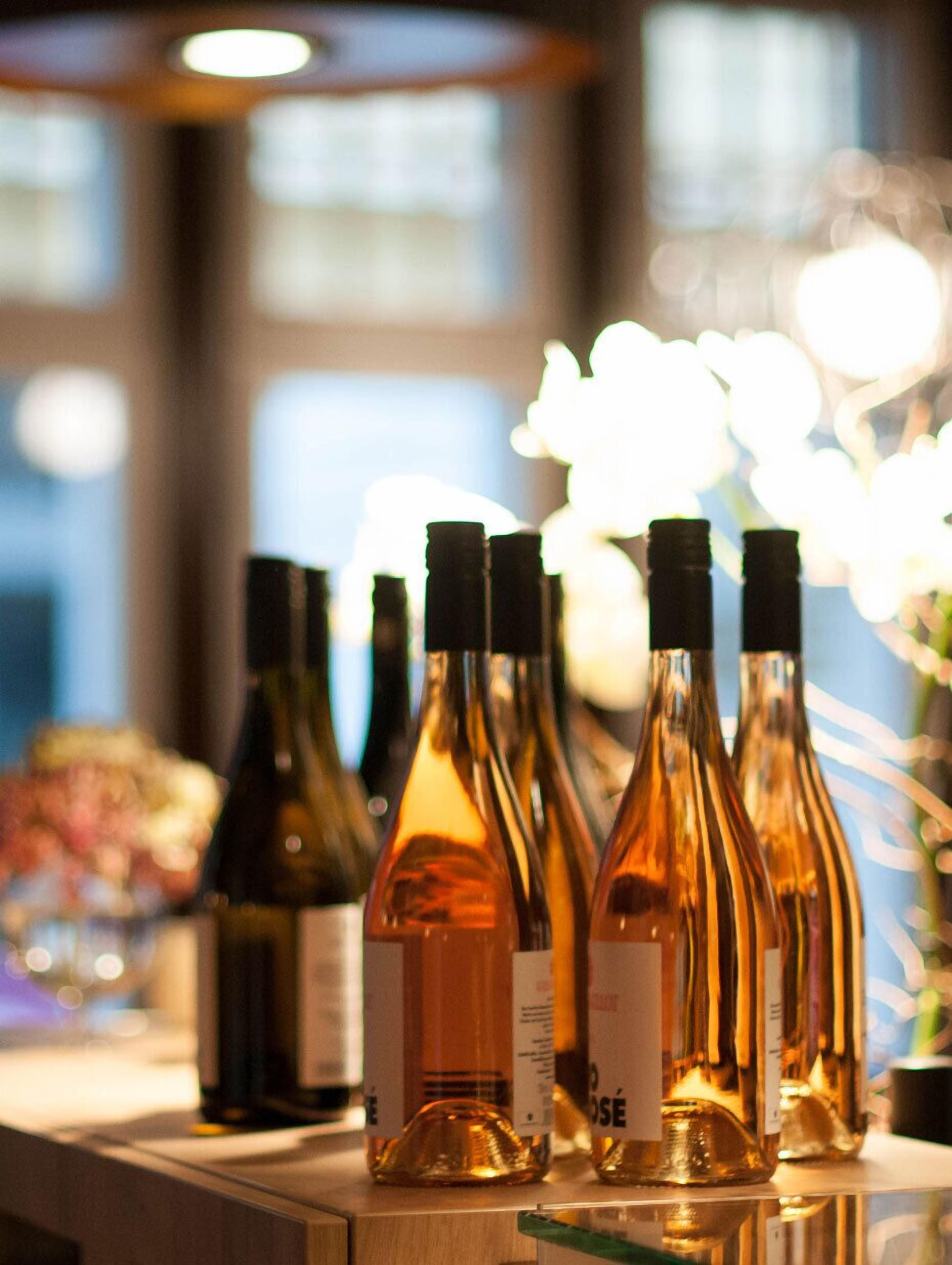 Varias botellas de vino sobre una encimera, con un fondo desenfocado de ventanas y luces.
