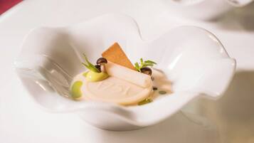 A dessert in a white, heart-shaped dish with a piece of cake, a dollop of cream, and a sprig of green herb.