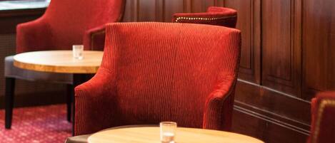 A hotel room with two red upholstered chairs and a round wooden table, each with a glass on it. The room has a red carpet and wooden paneling on the walls.