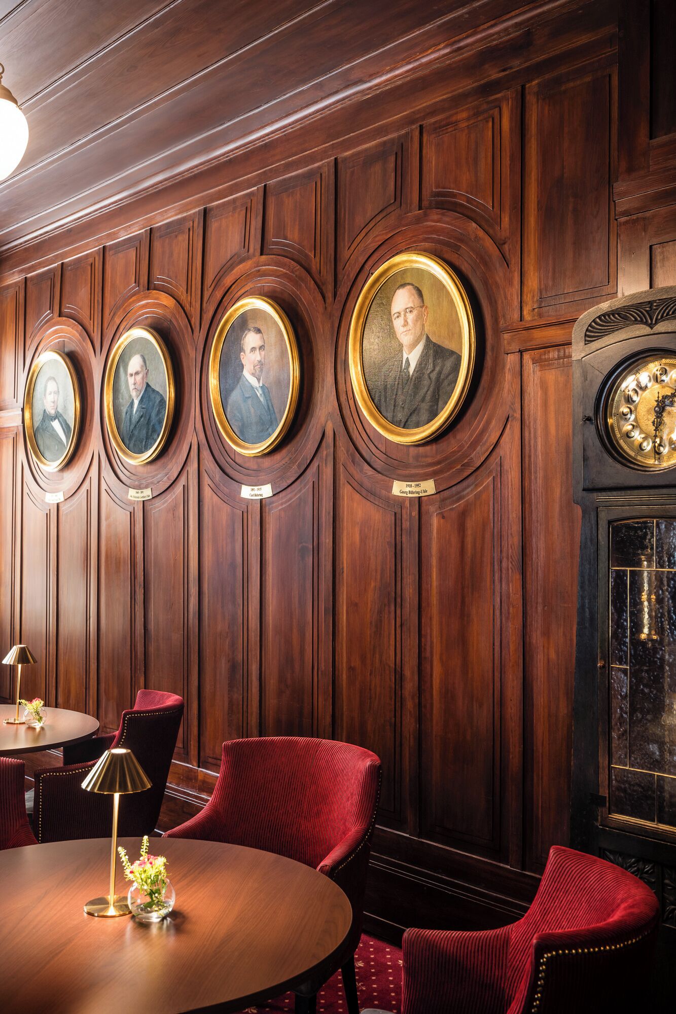 A room with wooden paneling, a round table with chairs, and a clock.