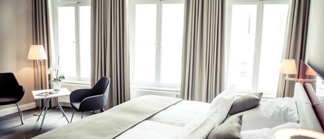 A hotel room with a large bed, two bedside tables, a chair, and a window with curtains.