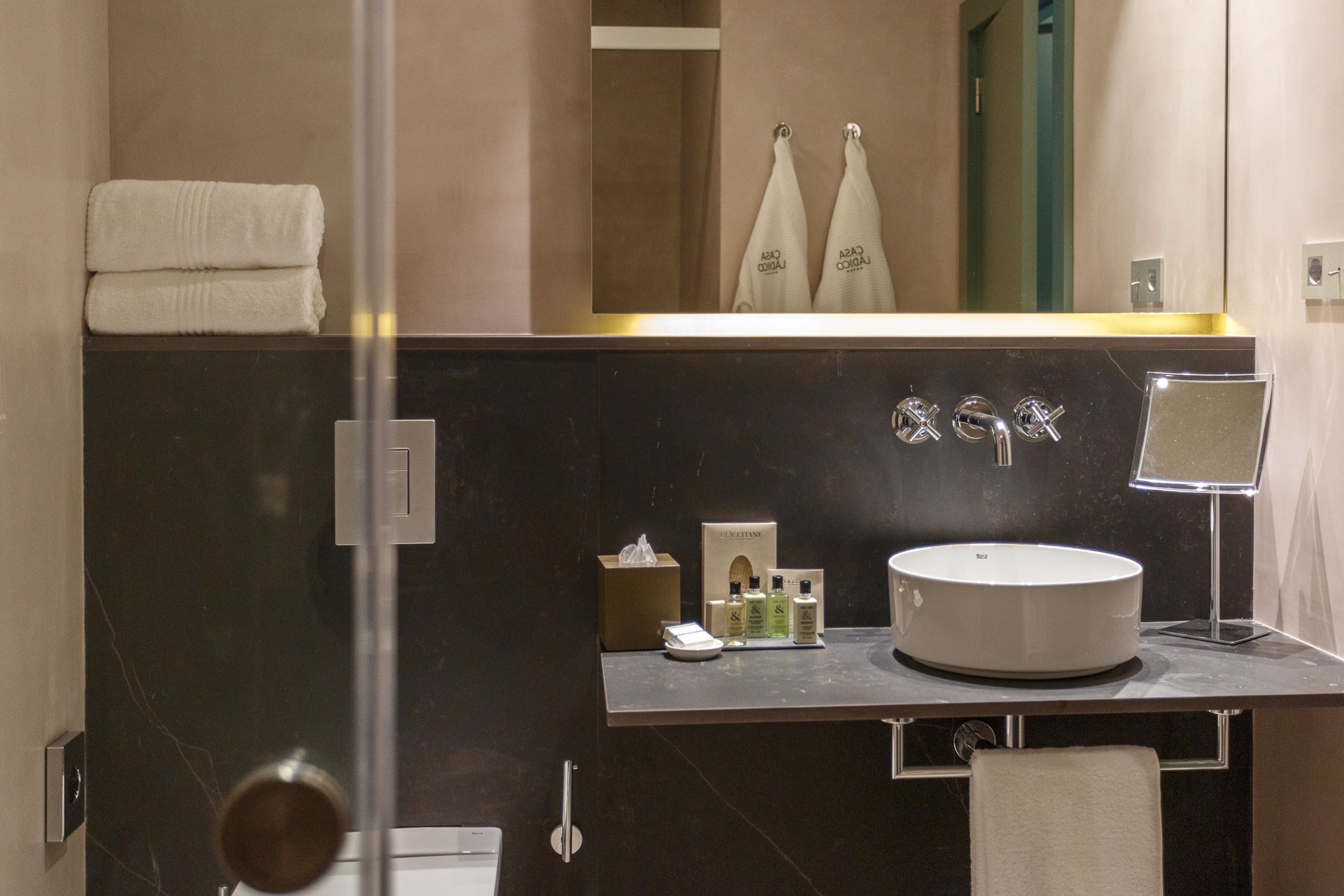 Un baño moderno con un espejo grande, un lavabo redondo y una cabina de ducha de vidrio.