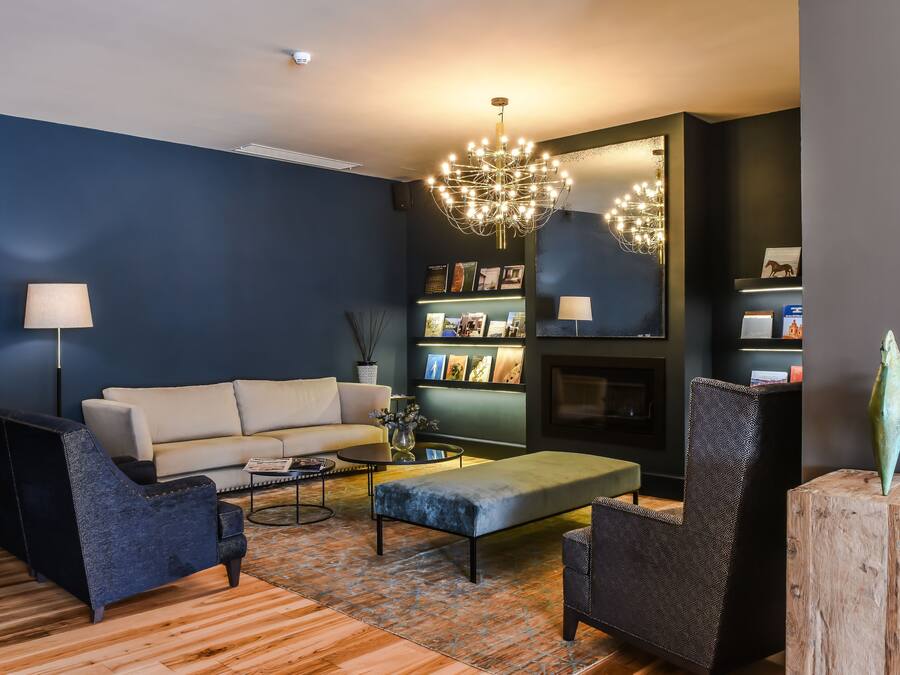 A modern living room with a dark blue accent wall, a white sofa, a patterned ottoman, and a unique chandelier.
