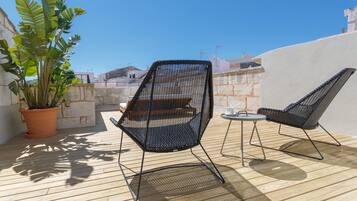 Une terrasse avec deux chaises en métal noir, une petite table ronde et un pot de fleurs.