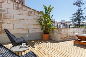 Une terrasse sur le toit, avec des chaises en osier, une table sur laquelle se trouvent une tasse et une soucoupe, et une plante en pot.