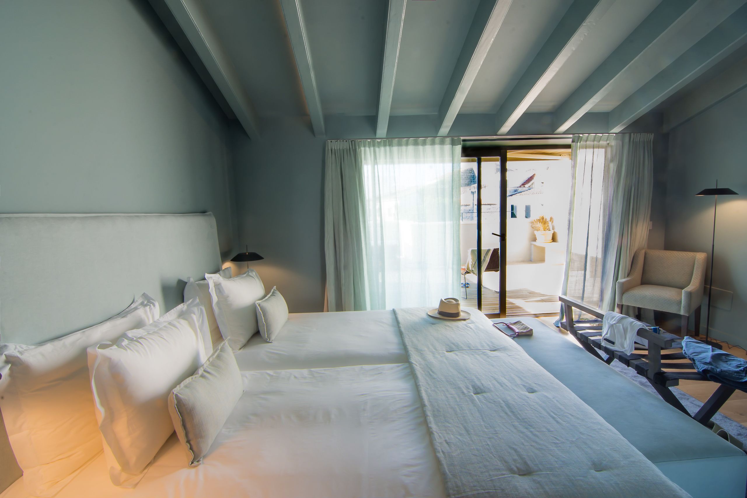 A hotel room with a large bed, a bench, a chair, and a view of the outside.