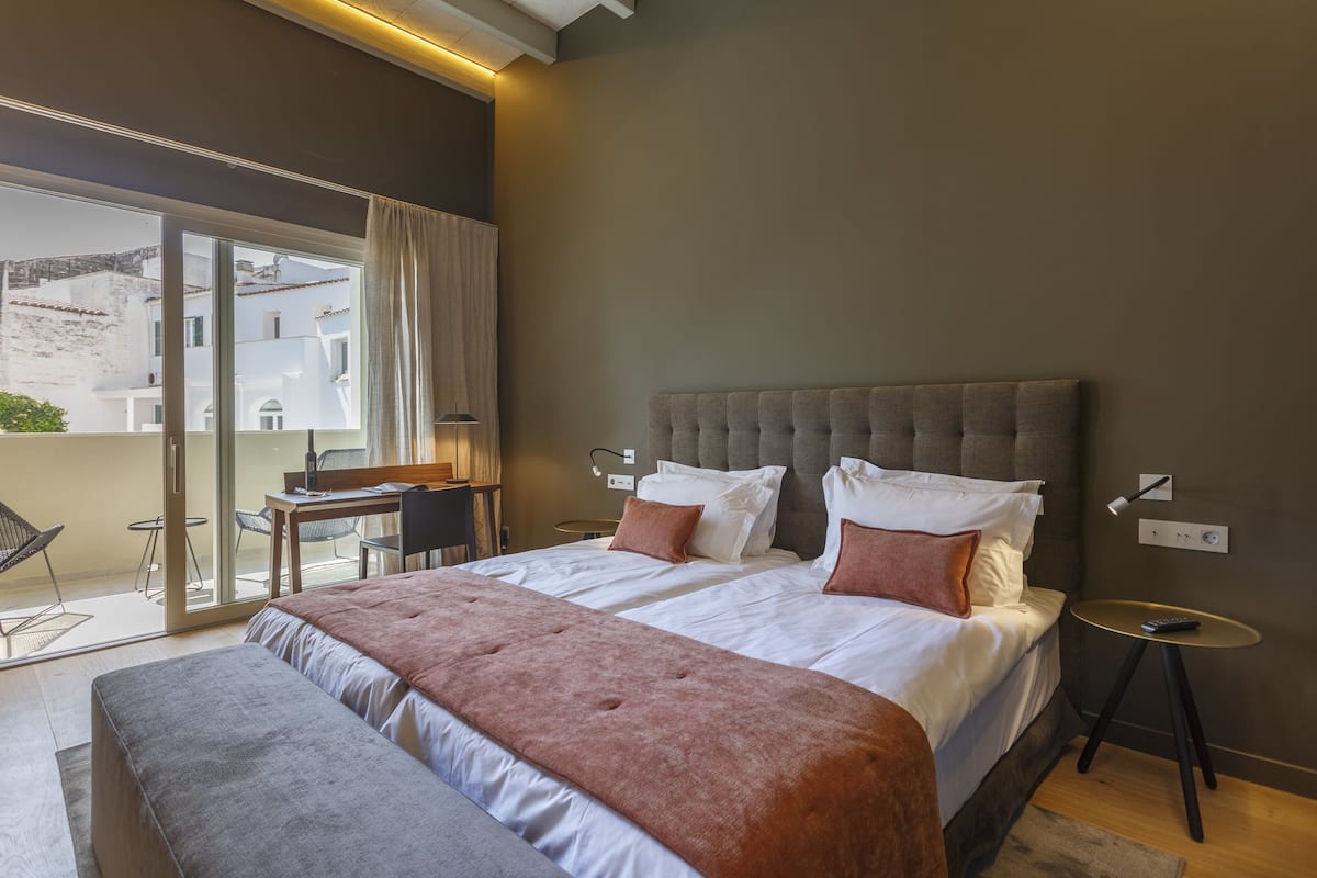 Een moderne hotelkamer met een groot bed, een bureau en een balkon met uitzicht op gebouwen.