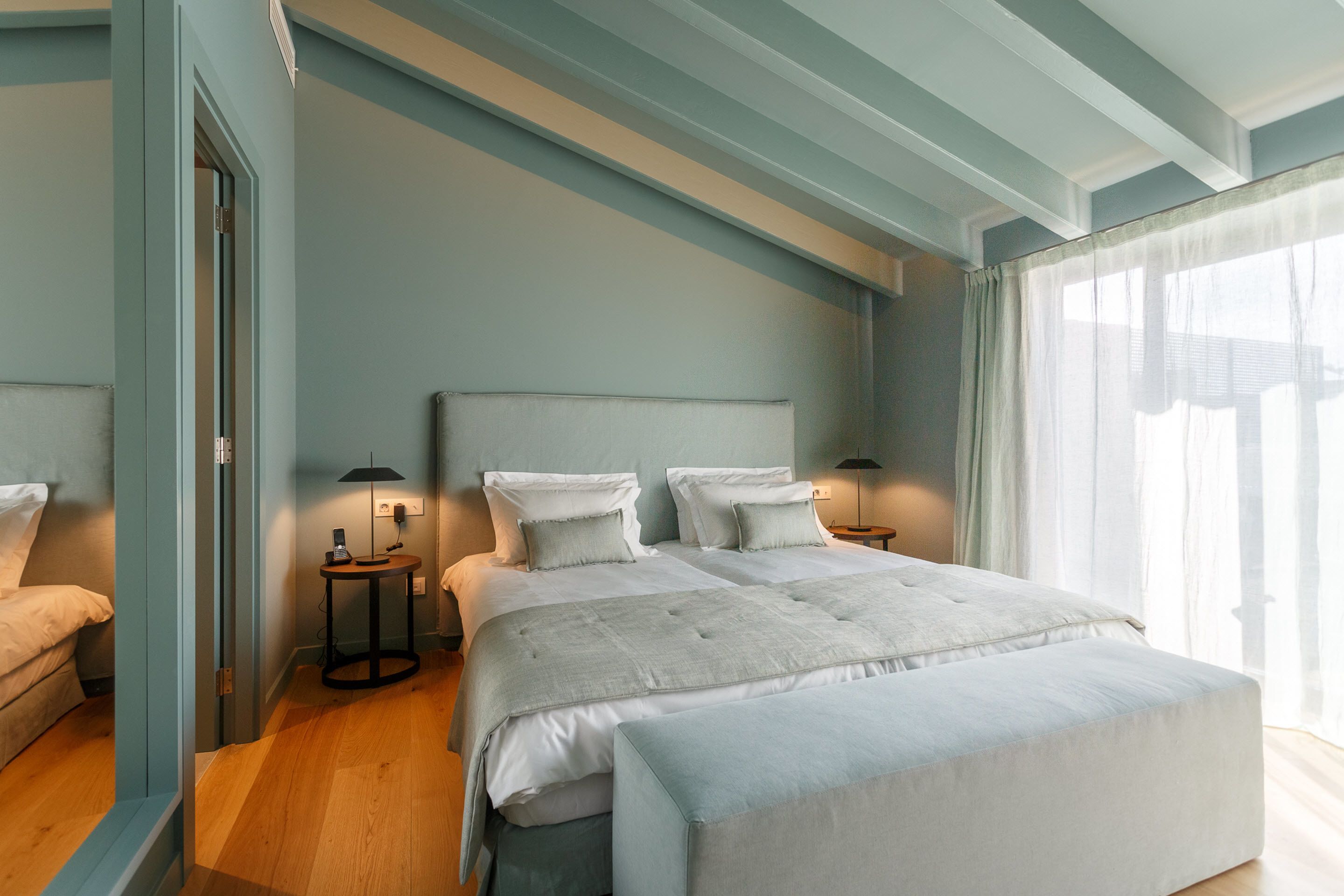 Un dormitorio con una cama grande, mesitas de noche y un ventanal con cortinas translúcidas.