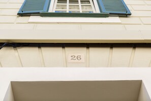 Une façade d’immeuble avec une fenêtre, des volets et une plaque numérotée.