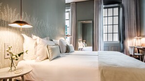A hotel room with a large bed, two bedside tables, a round table, and a view of the city through a window. -  Bordoy Casa Ládico - Hotel Boutique Adults Only (Mahón)