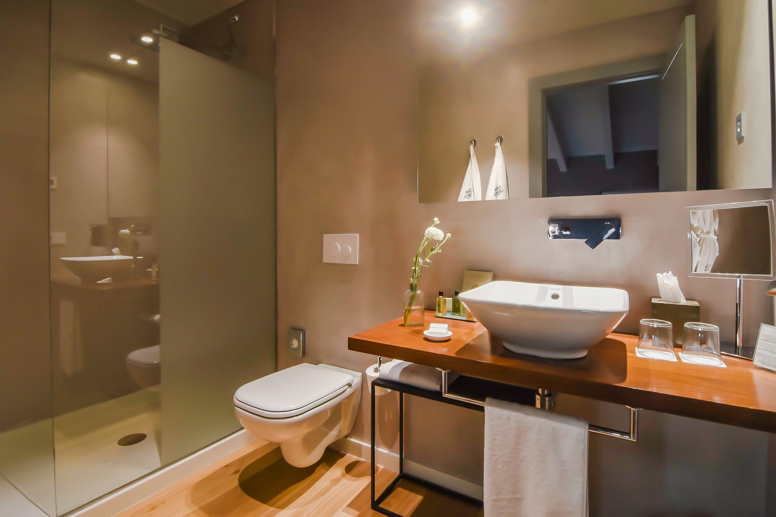A modern bathroom with a glass-enclosed shower, a white toilet, and a wooden vanity with a large sink.