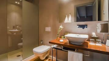 Un baño moderno con ducha envuelta en vidrio, inodoro blanco y tocador de madera con un lavamanos grande.