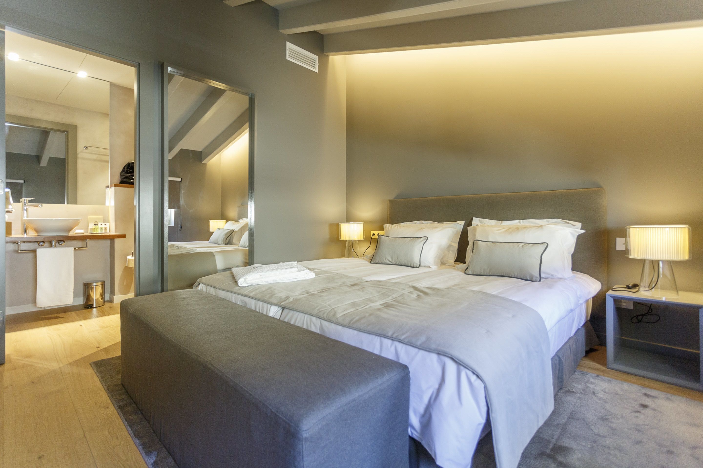 Un dormitorio moderno con una cama grande, mesitas de noche, un banco y un espejo.