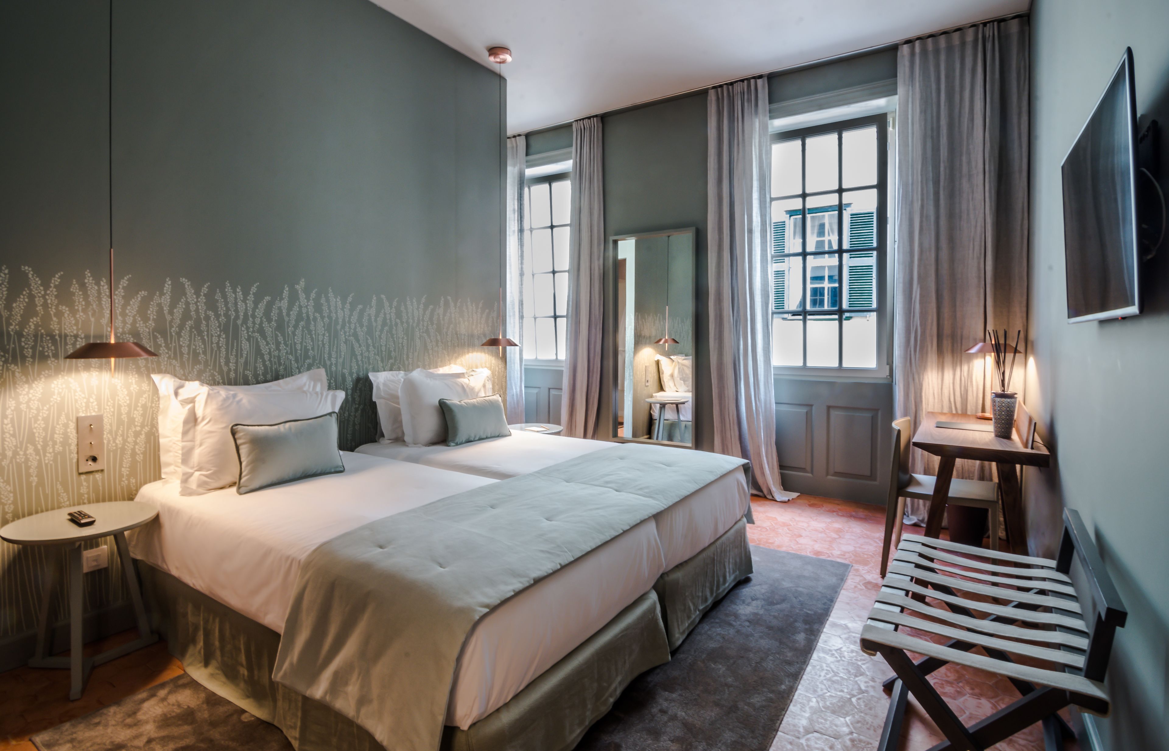 A neatly arranged bedroom with a large bed, bedside tables, a small desk, and a chair.