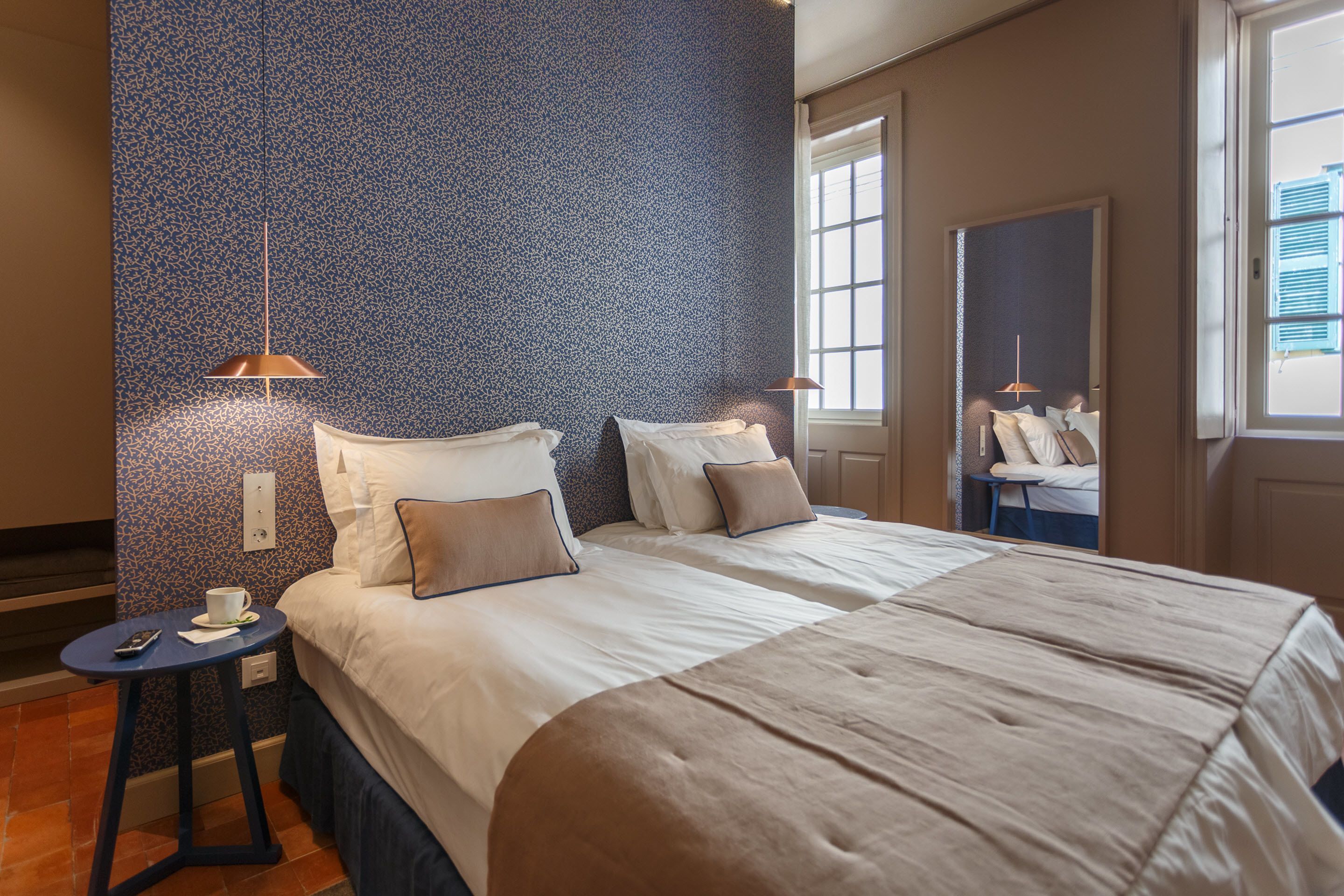 A hotel room with two beds, a small table, and a window.