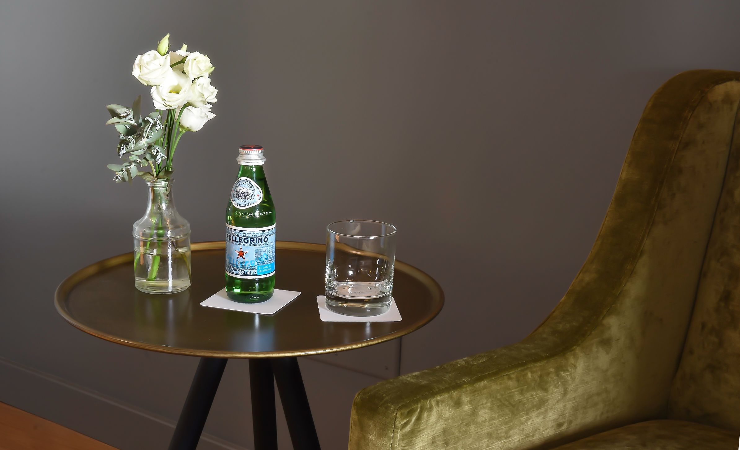 A small round table with a bottle of Pellegrino water, a glass, and a vase with white flowers.