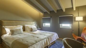 Un dormitorio con una cama grande, dos mesitas de noche, una silla y dos ventanas con persianas.