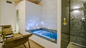 A spa room with a hot tub, a seating area with a chair and a small table, and a shower area with a glass door. -  Bordoy Casa Ládico - Hotel Boutique Adults Only (Mahón)